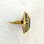 Vintage gold tone Belle Époque style ring with oval sapphire blue glass center stone, paste halo, and black enamel carved detailing