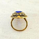 Vintage gold tone Belle Époque style ring with oval sapphire blue glass center stone, paste halo, and black enamel carved detailing