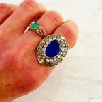 Vintage gold tone Belle Époque style ring with oval sapphire blue glass center stone, paste halo, and black enamel carved detailing