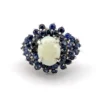 Oval natural opal surrounded by tiered blue sapphires in a white gold plated sterling silver princess cluster ring