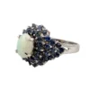 Oval natural opal surrounded by tiered blue sapphires in a white gold plated sterling silver princess cluster ring