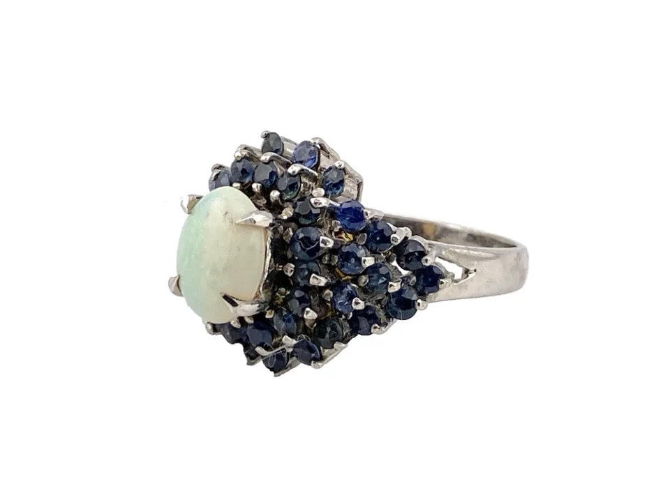 Oval natural opal surrounded by tiered blue sapphires in a white gold plated sterling silver princess cluster ring