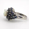 Oval natural opal surrounded by tiered blue sapphires in a white gold plated sterling silver princess cluster ring