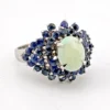 Oval natural opal surrounded by tiered blue sapphires in a white gold plated sterling silver princess cluster ring