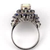 Oval natural opal surrounded by tiered blue sapphires in a white gold plated sterling silver princess cluster ring