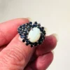 Oval natural opal surrounded by tiered blue sapphires in a white gold plated sterling silver princess cluster ring