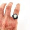 Oval natural opal surrounded by tiered blue sapphires in a white gold plated sterling silver princess cluster ring
