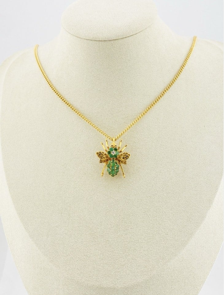 Gold-plated sterling silver bee brooch with a green gemstone-set body, clear cubic zirconia accent, raised patterned wings, and textured legs.