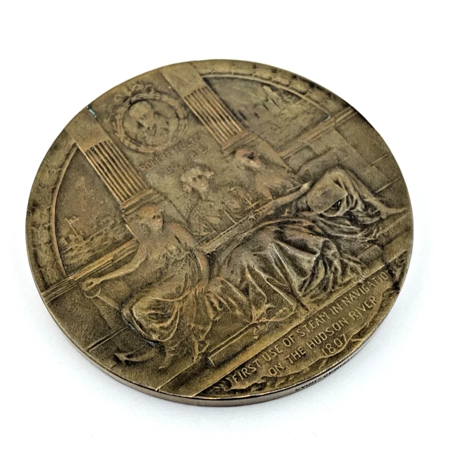 1909 Hudson-Fulton bronze medal showing Robert Fulton’s portrait above three seated allegorical women and a model steamboat.