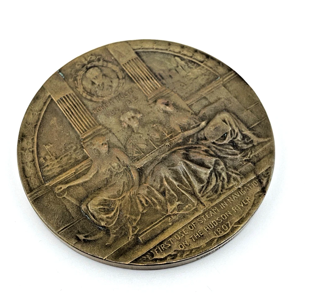 1909 Hudson-Fulton bronze medal showing Robert Fulton’s portrait above three seated allegorical women and a model steamboat.