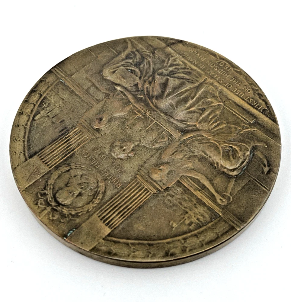 1909 Hudson-Fulton bronze medal showing Robert Fulton’s portrait above three seated allegorical women and a model steamboat.