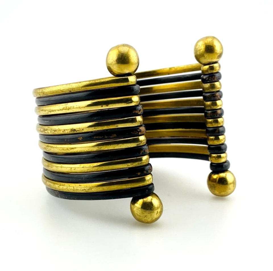 Wide cuff bracelet with alternating golden brass and near-black copper bands, four round brass finials, and small areas of wear to the darkened finish.