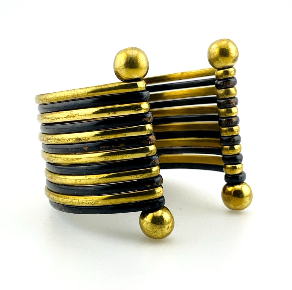 Wide cuff bracelet with alternating golden brass and near-black copper bands, four round brass finials, and small areas of wear to the darkened finish.