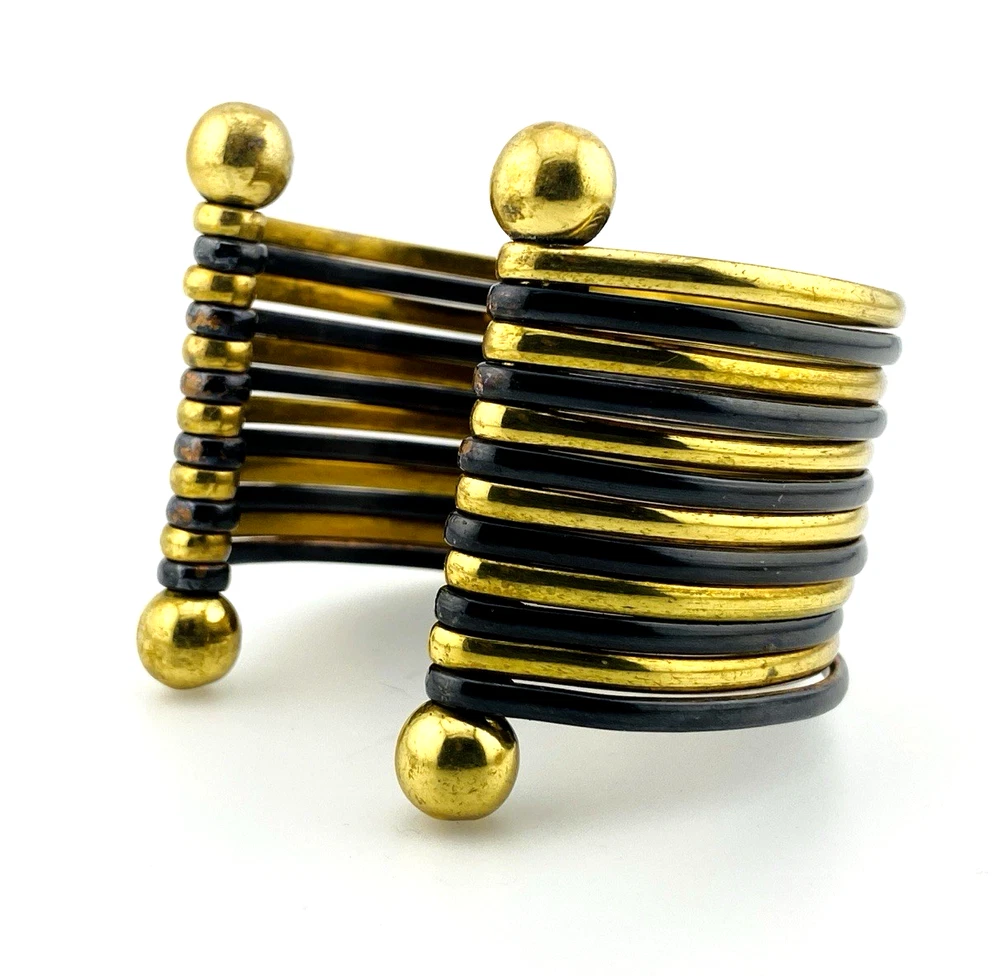 Wide cuff bracelet with alternating golden brass and near-black copper bands, four round brass finials, and small areas of wear to the darkened finish.