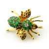 Gold-plated sterling silver bee brooch with a green gemstone-set body, clear cubic zirconia accent, raised patterned wings, and textured legs.
