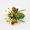 Gold-plated sterling silver bee brooch with a green gemstone-set body, clear cubic zirconia accent, raised patterned wings, and textured legs.