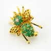 Gold-plated sterling silver bee brooch with a green gemstone-set body, clear cubic zirconia accent, raised patterned wings, and textured legs.