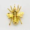 Gold-plated sterling silver bee brooch with a green gemstone-set body, clear cubic zirconia accent, raised patterned wings, and textured legs.