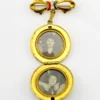 Gold-plated WWII sweetheart locket brooch with an eagle-and-shield emblem on mother of pearl, engraved border, and red, white, and blue enameled bow.