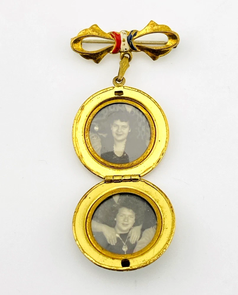 Gold-plated WWII sweetheart locket brooch with an eagle-and-shield emblem on mother of pearl, engraved border, and red, white, and blue enameled bow.