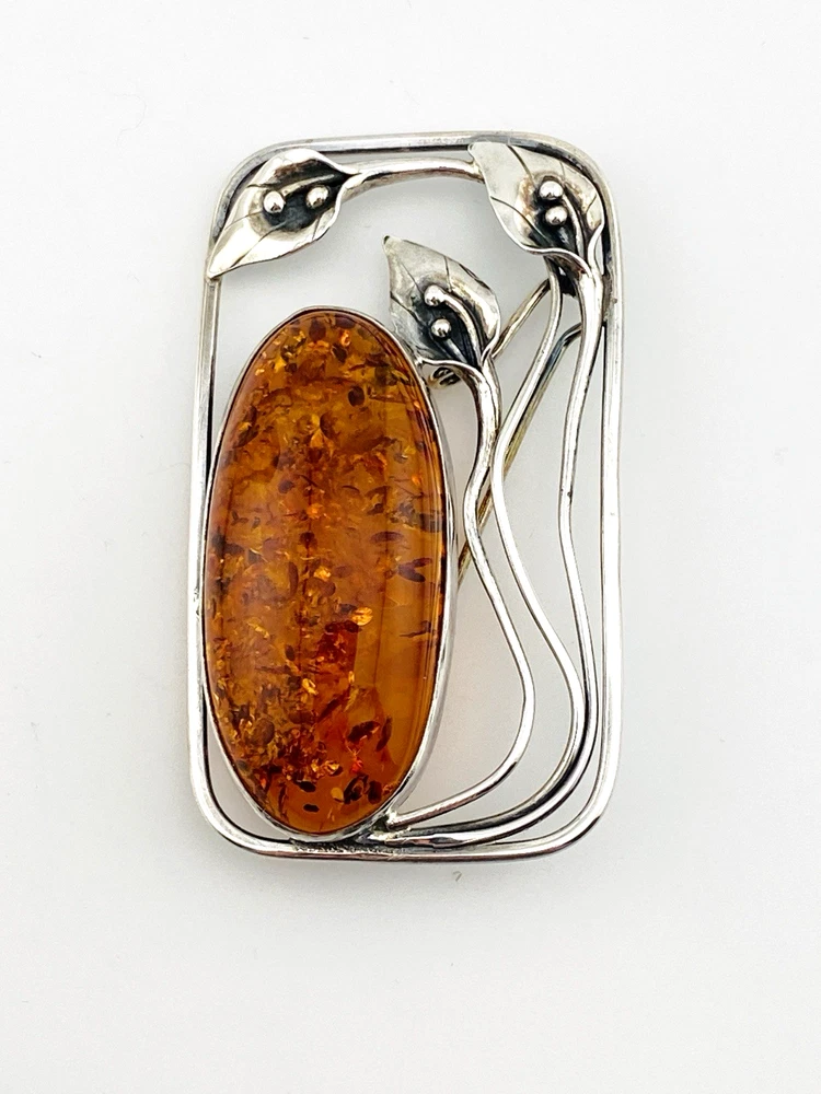 Circa 1990s sterling silver brooch with a large oval cognac amber cabochon and three calla lilies forming an open rectangular frame.