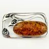 Circa 1990s sterling silver brooch with a large oval cognac amber cabochon and three calla lilies forming an open rectangular frame.