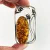 Circa 1990s sterling silver brooch with a large oval cognac amber cabochon and three calla lilies forming an open rectangular frame.