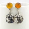 Amber stud earrings with dangling sterling silver flowers, showing one golden yellow cabochon and one deeper orange cabochon.