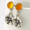 Amber stud earrings with dangling sterling silver flowers, showing one golden yellow cabochon and one deeper orange cabochon.