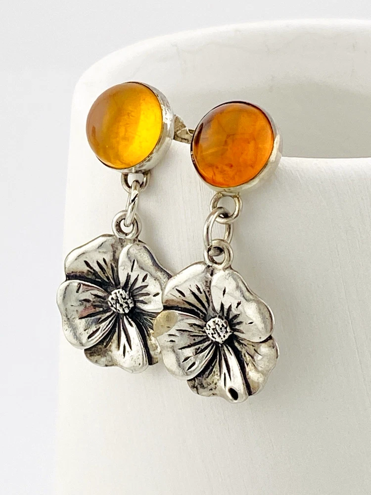 Amber stud earrings with dangling sterling silver flowers, showing one golden yellow cabochon and one deeper orange cabochon.