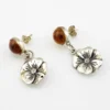Amber stud earrings with dangling sterling silver flowers, showing one golden yellow cabochon and one deeper orange cabochon.