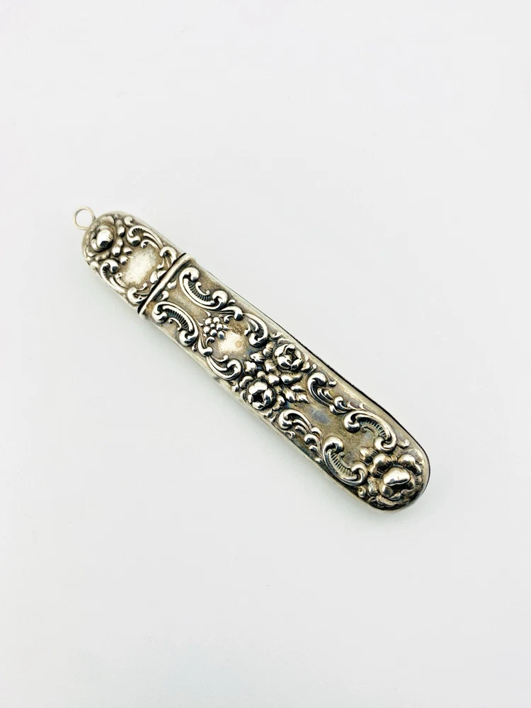 Vintage sterling silver needle case with raised cabbage roses, curling scrollwork, darkened recesses, and a suspension loop on the cap.