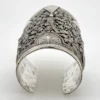 Wide peaked silver cuff with three crowned celestial dancers, openwork leafy scrolls and a rounded longevity medallion