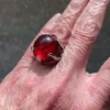 High-domed red glass cabochon ring with broad silver prongs, fleur-de-lis shoulders and an overlapping adjustable band