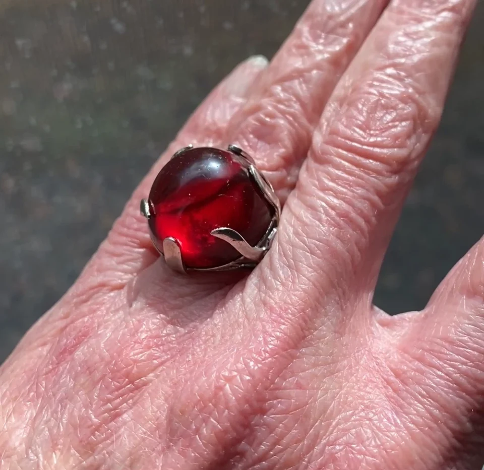 High-domed red glass cabochon ring with broad silver prongs, fleur-de-lis shoulders and an overlapping adjustable band