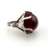 High-domed red glass cabochon ring with broad silver prongs, fleur-de-lis shoulders and an overlapping adjustable band