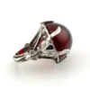 High-domed red glass cabochon ring with broad silver prongs, fleur-de-lis shoulders and an overlapping adjustable band