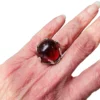 High-domed red glass cabochon ring with broad silver prongs, fleur-de-lis shoulders and an overlapping adjustable band