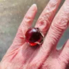 High-domed red glass cabochon ring with broad silver prongs, fleur-de-lis shoulders and an overlapping adjustable band
